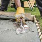 Close up on worker paving or smoothing fresh concrete in plywood walls to be used for an outdoor patio, driveway or sidewalk.