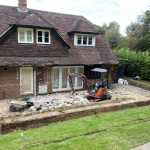 small digger breaking up existing patio outside the back of a brick house